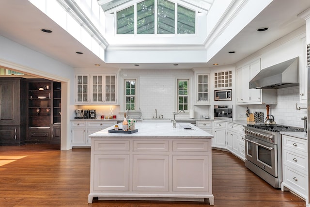 10 Sunny Ridge Rd, Washington, CT 06793 - kitchen featuring appliances with stainless steel finishes, wall chimney exhaust hood, backsplash, white cabinets, and an island with sink