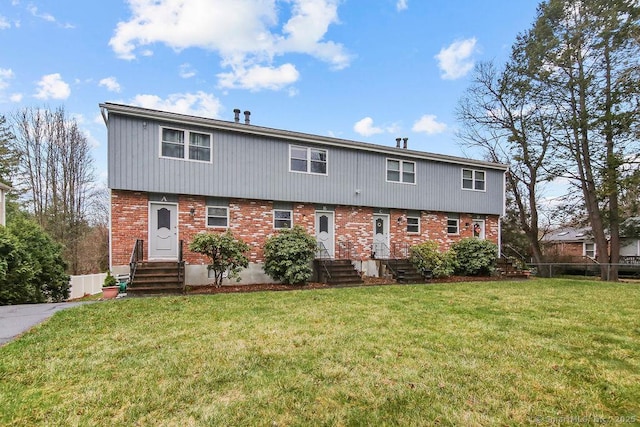 view of front facade with entry steps, a front yard, fence, and brick siding
