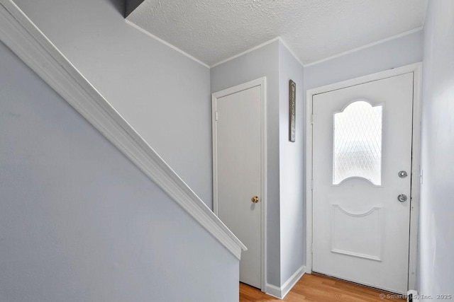 foyer with light wood-style flooring, a textured ceiling, and crown molding