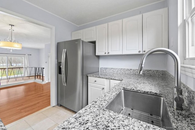kitchen with stainless steel fridge with ice dispenser, white cabinetry, a sink, and light stone counters