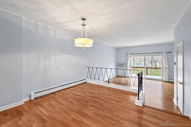 empty room with a textured ceiling, wood finished floors, and a baseboard heating unit