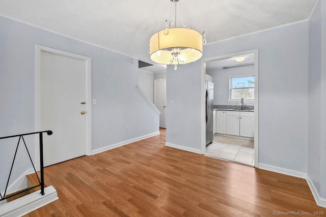 unfurnished dining area featuring baseboards, light wood-type flooring, and a sink