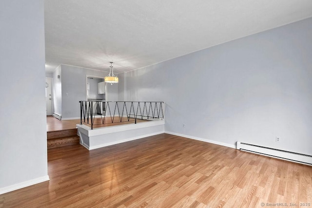 empty room featuring a baseboard radiator, wood finished floors, and baseboards