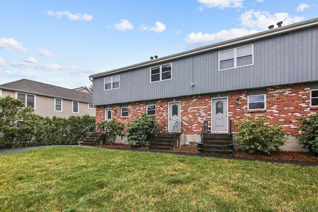 back of property with entry steps, brick siding, and a lawn