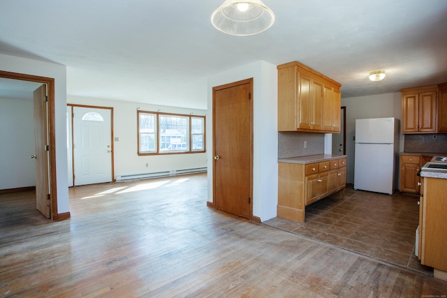 kitchen featuring light countertops, a baseboard heating unit, decorative backsplash, freestanding refrigerator, and wood finished floors