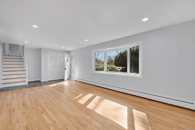 unfurnished living room featuring wood finished floors, stairway, a baseboard heating unit, and recessed lighting