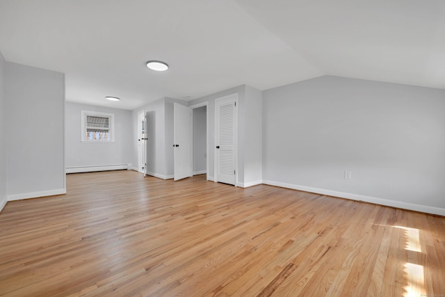 unfurnished room with a baseboard radiator, light wood finished floors, baseboards, and lofted ceiling
