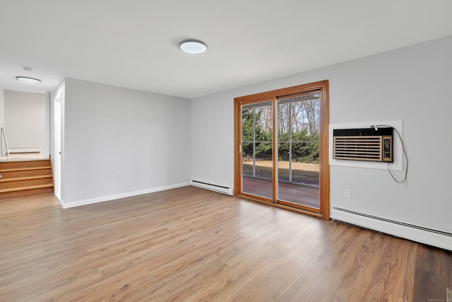 empty room with stairs, a baseboard heating unit, a wall unit AC, and wood finished floors