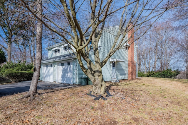 exterior space featuring an attached garage, a chimney, and aphalt driveway
