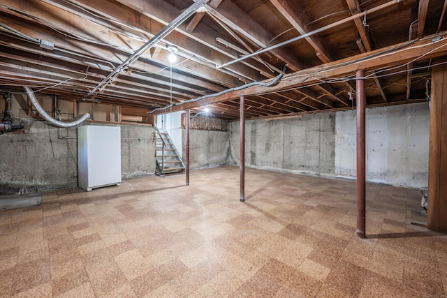 unfinished below grade area featuring tile patterned floors, freestanding refrigerator, and stairs