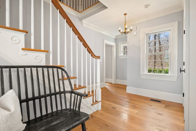 entrance foyer featuring stairway, ornamental molding, a chandelier, light wood-style floors, and visible vents