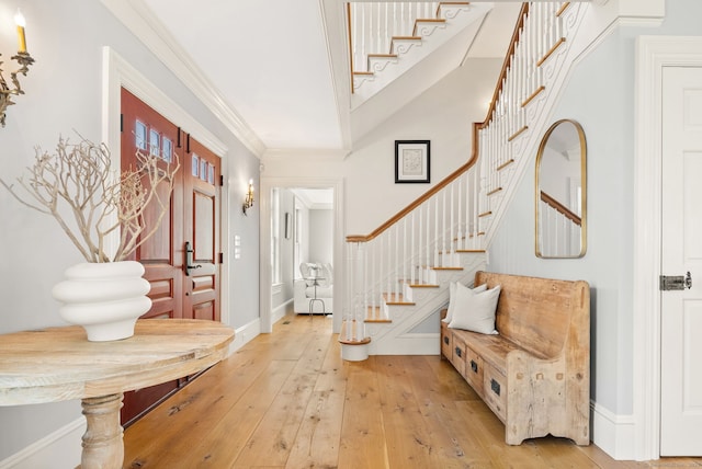 entrance foyer with light wood-style flooring, crown molding, baseboards, and stairs