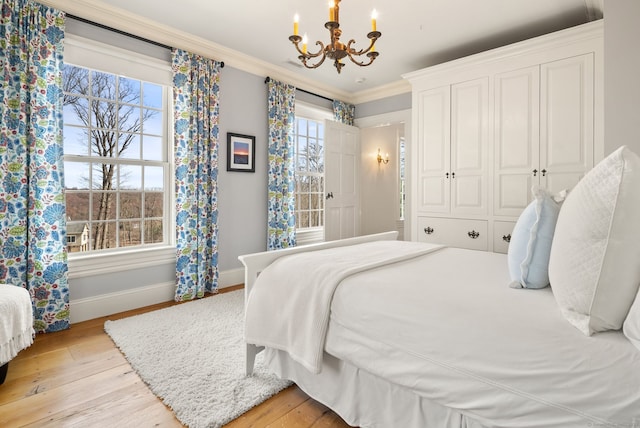 bedroom featuring light wood finished floors, baseboards, crown molding, and an inviting chandelier