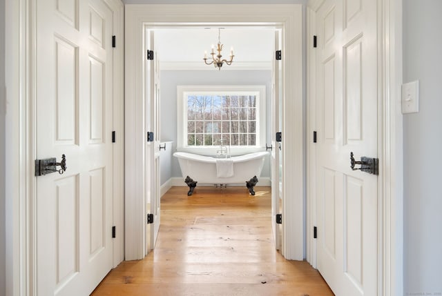 hall with baseboards, ornamental molding, light wood-style flooring, and an inviting chandelier