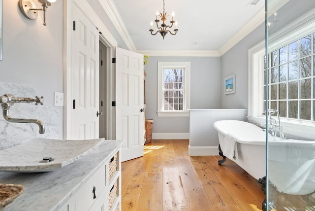 bathroom with hardwood / wood-style flooring, a chandelier, a soaking tub, baseboards, and ornamental molding