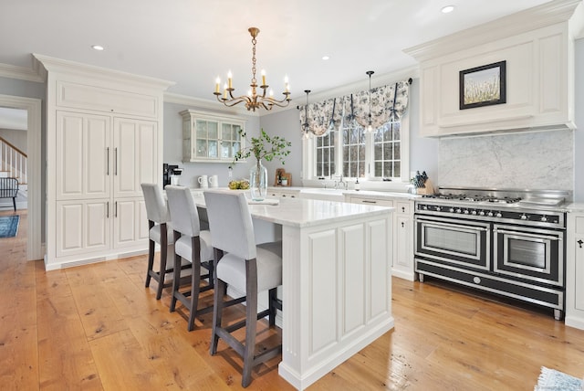kitchen with light wood-style flooring, a chandelier, crown molding, glass insert cabinets, and range with two ovens