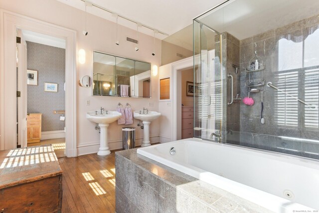 bathroom with wallpapered walls, hardwood / wood-style flooring, tiled tub, and a tile shower