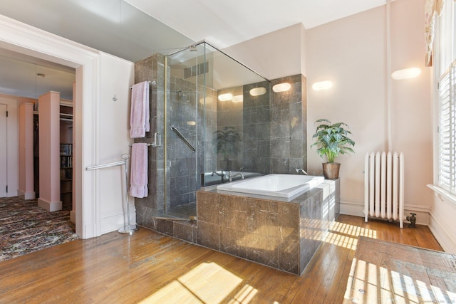 bathroom with a bath, hardwood / wood-style flooring, a stall shower, radiator, and a spacious closet