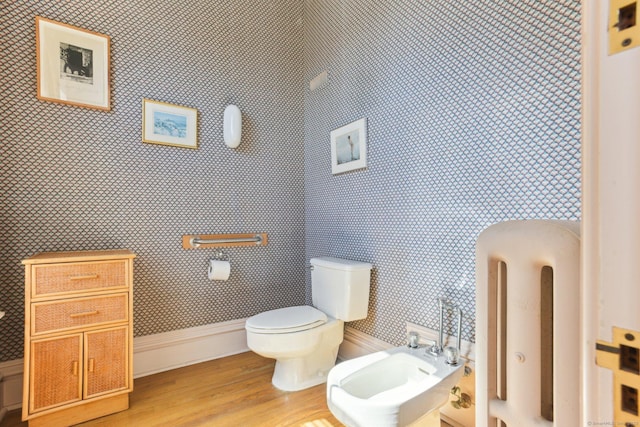 bathroom with baseboards, wallpapered walls, toilet, wood finished floors, and a bidet