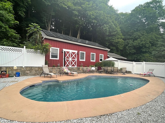 view of swimming pool featuring a patio, an outbuilding, a fenced in pool, a fenced backyard, and a forest view
