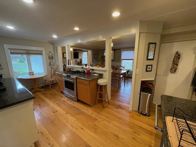 kitchen with recessed lighting, light wood-style flooring, dark stone counters, brown cabinetry, and stainless steel range with gas cooktop