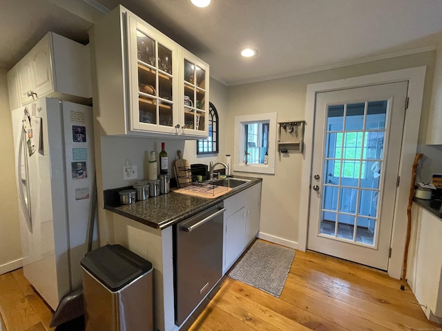 kitchen featuring light wood finished floors, glass insert cabinets, dark countertops, dishwasher, and freestanding refrigerator