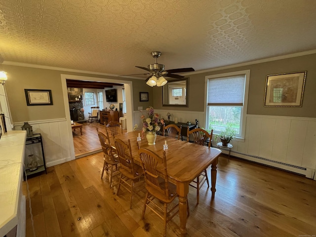 dining space featuring hardwood / wood-style floors, a wainscoted wall, ceiling fan, and a baseboard heating unit