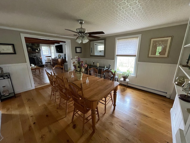 dining room featuring a baseboard heating unit, ornamental molding, ceiling fan, a wainscoted wall, and light wood finished floors