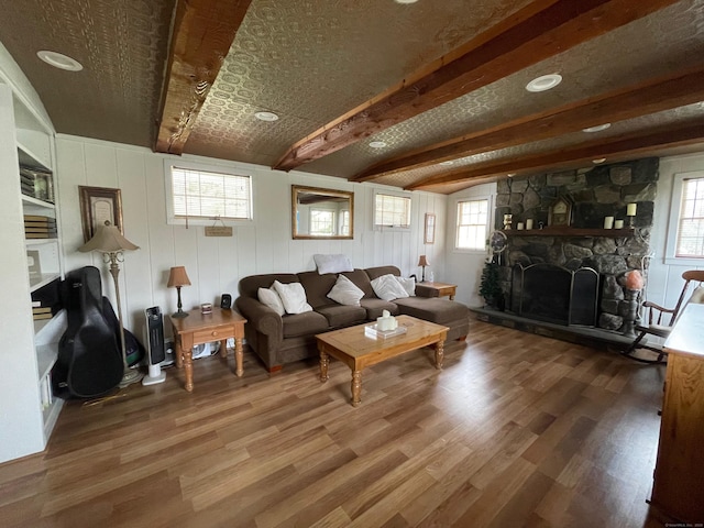 living area with a fireplace, beam ceiling, and wood finished floors