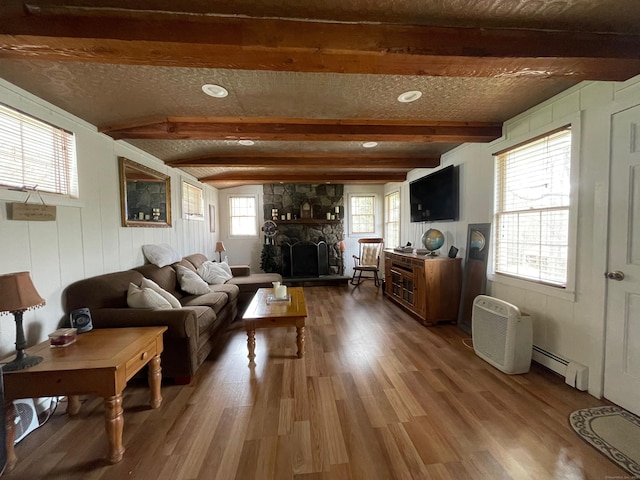 living room featuring recessed lighting, wood finished floors, beamed ceiling, baseboard heating, and a stone fireplace