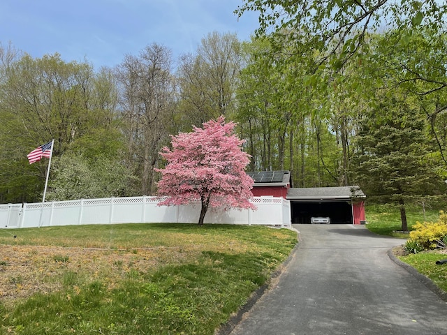 view of side of home featuring fence, driveway, a yard, and roof mounted solar panels