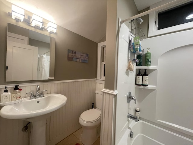 bathroom with tile patterned floors, vaulted ceiling, shower / bath combo with shower curtain, a wainscoted wall, and toilet