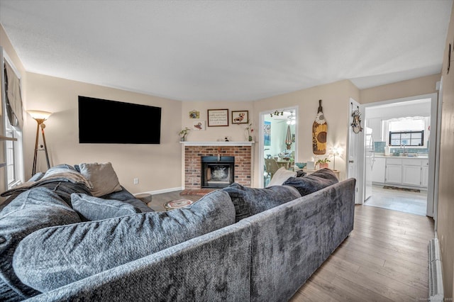 living area with baseboards, a brick fireplace, and hardwood / wood-style flooring