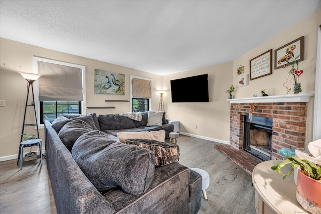 living area featuring baseboards, a textured ceiling, wood finished floors, and a brick fireplace