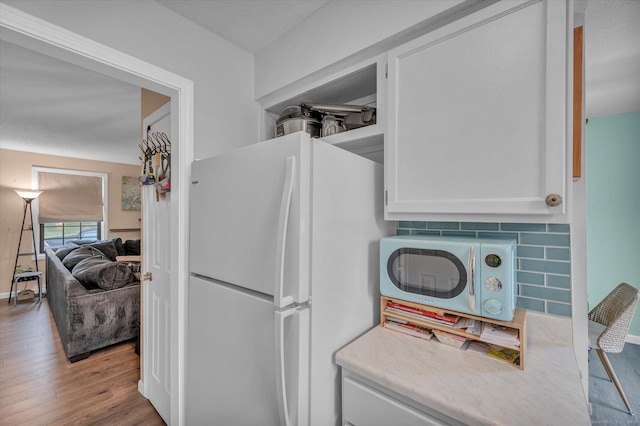 kitchen featuring white cabinets, light countertops, wood finished floors, backsplash, and freestanding refrigerator