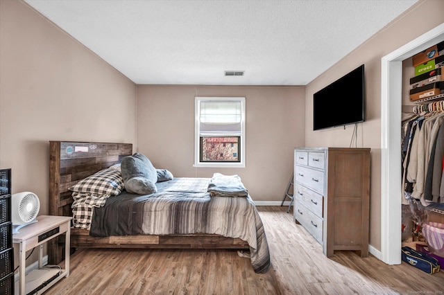 bedroom with baseboards, a textured ceiling, visible vents, and light wood-style floors