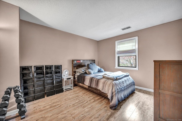 bedroom with baseboards, visible vents, wood finished floors, and a textured ceiling