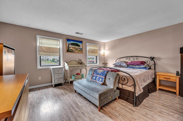 bedroom featuring baseboards, visible vents, light wood-style floors, and a textured ceiling