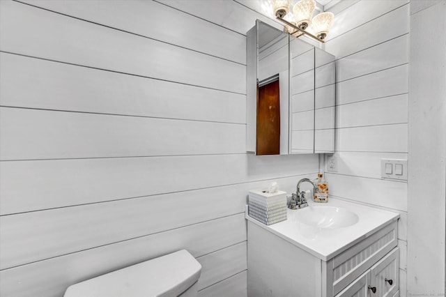 bathroom with toilet, wooden walls, a chandelier, and vanity