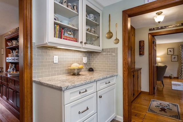 bar featuring light wood-type flooring, baseboards, and backsplash