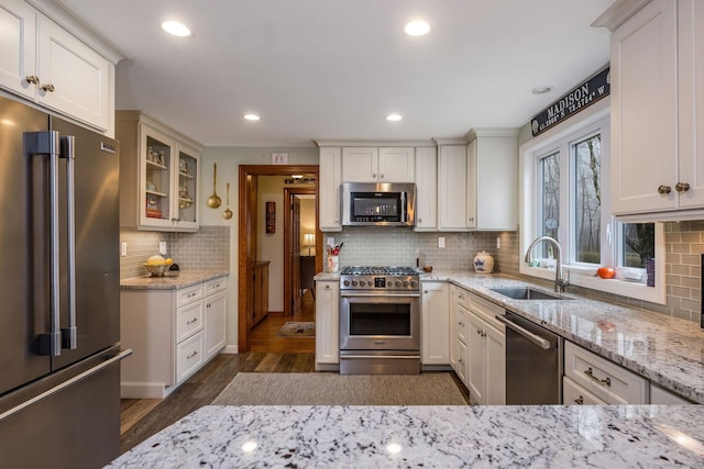 kitchen with dark wood finished floors, light stone countertops, tasteful backsplash, high end appliances, and a sink