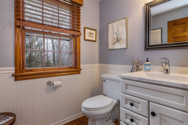 half bathroom with vanity, wainscoting, toilet, and wood finished floors