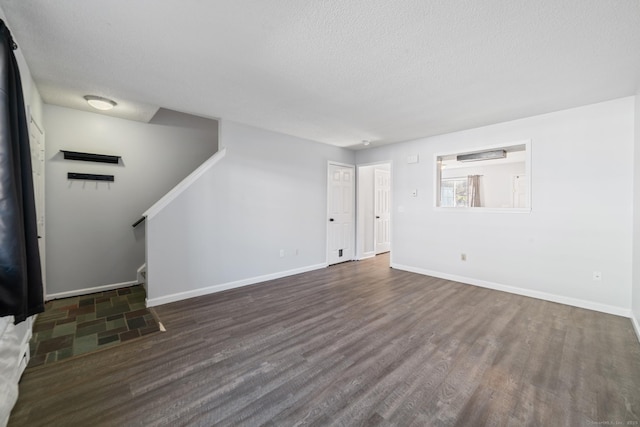 unfurnished living room with stairs, a textured ceiling, baseboards, and wood finished floors