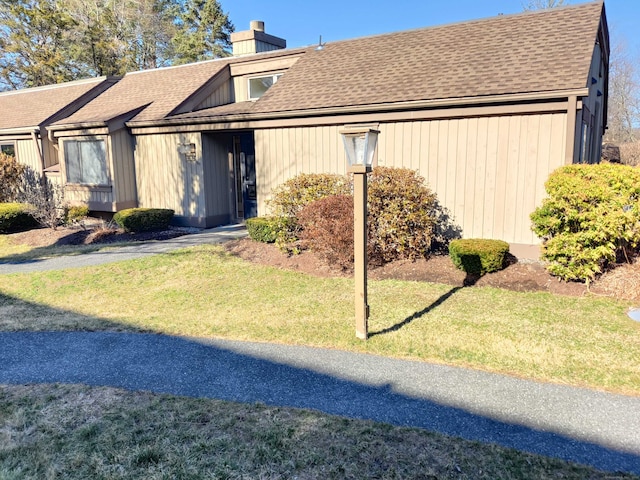 view of front of property with a shingled roof, a chimney, and a front yard