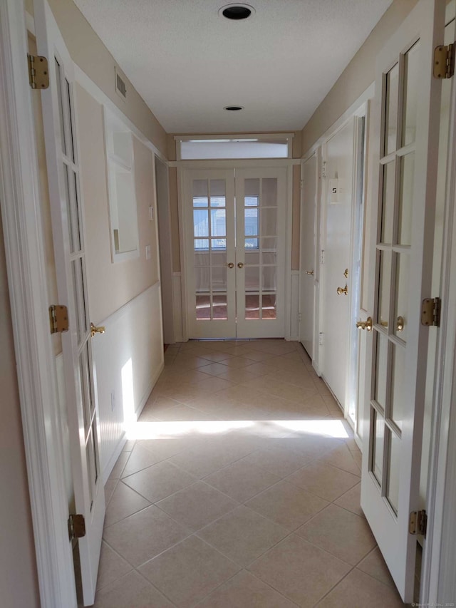 hallway featuring visible vents, french doors, and light tile patterned floors