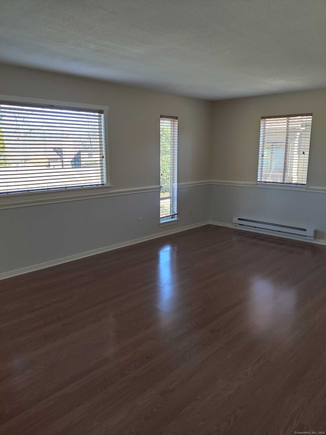 unfurnished room featuring baseboards, dark wood-style flooring, and a baseboard heating unit