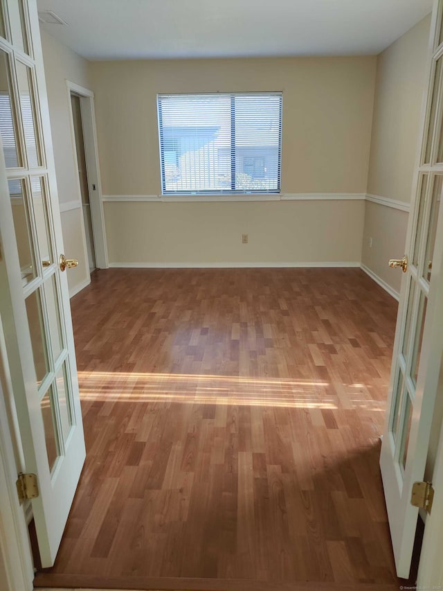 spare room featuring french doors, light wood-style flooring, and baseboards