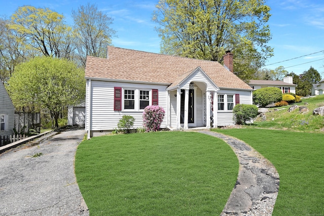view of front of property with a shingled roof, a garage, a front yard, an outbuilding, and a chimney