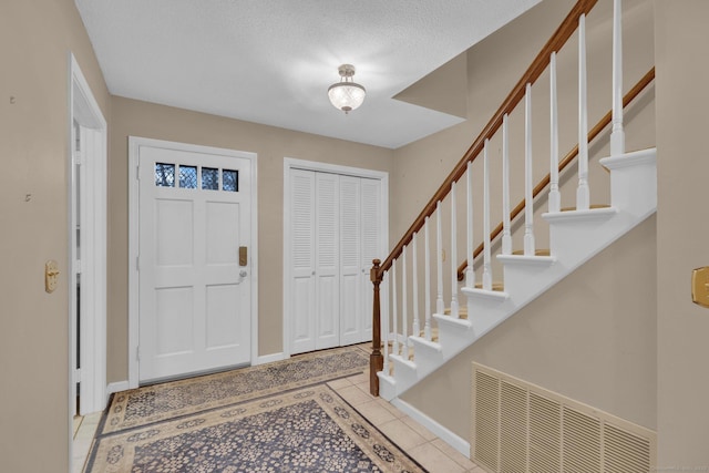 tiled foyer entrance featuring baseboards, visible vents, and stairway