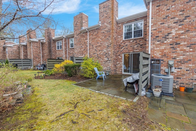 rear view of house featuring a patio area, a yard, a chimney, cooling unit, and brick siding